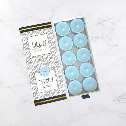 A set of blue tea-light candles presented in an open drawer-style box with a black and white geometric pattern design. The candles are displayed neatly inside the box.